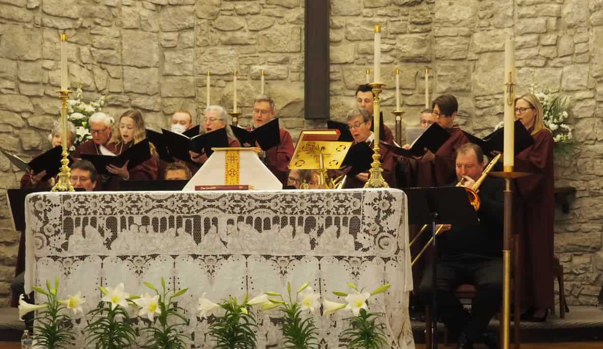 Choir singing at Calvary Episcopal Church altar with candles and stone wall backdrop.