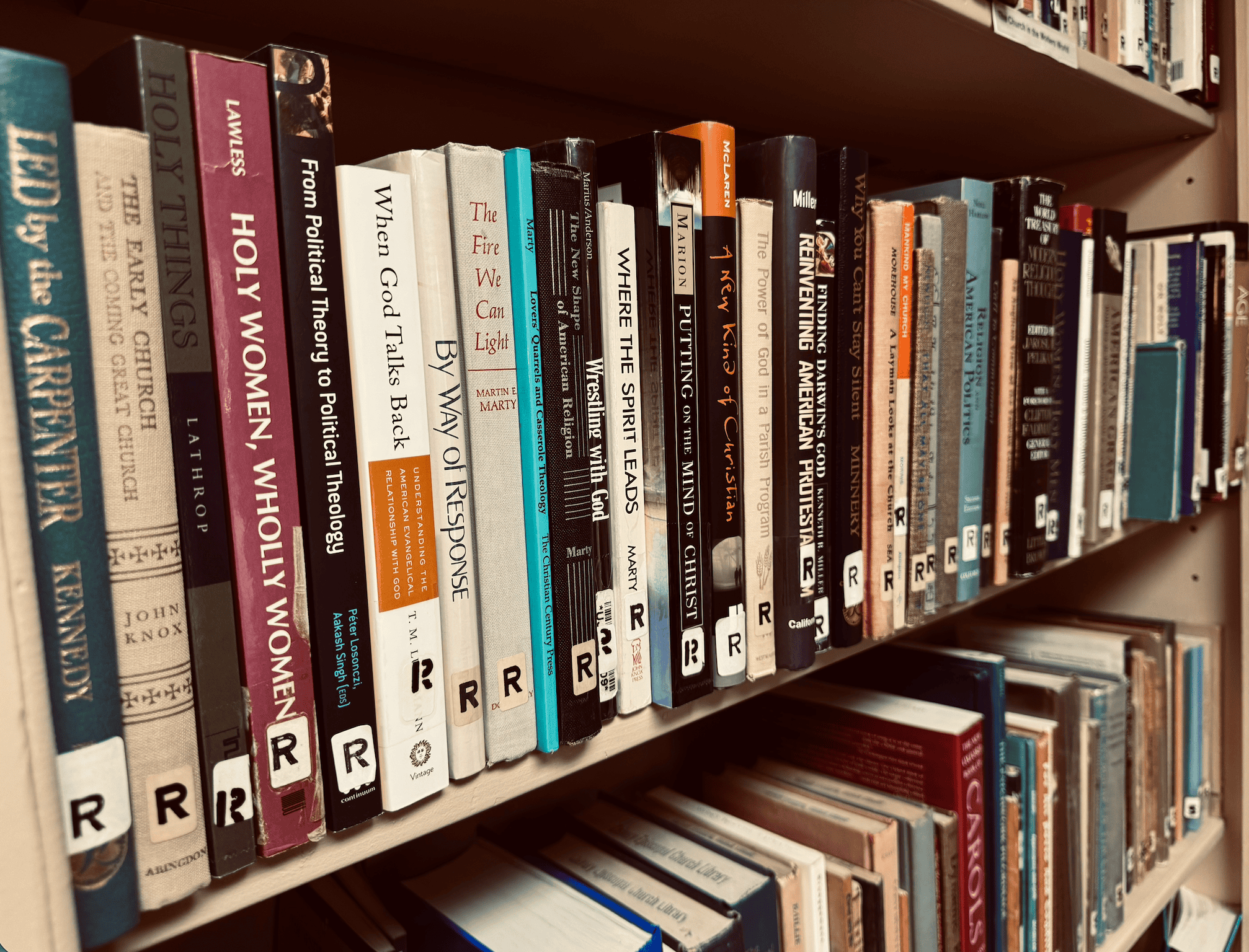 Books on a library shelf, including titles related to religion, theology, an.